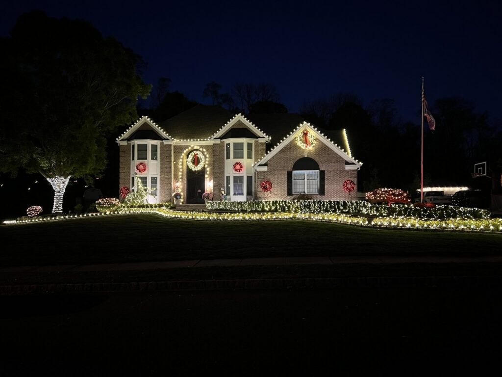 Brick house outlined in warm white C9 lights, with lit wreaths and wrapped shrubs at night