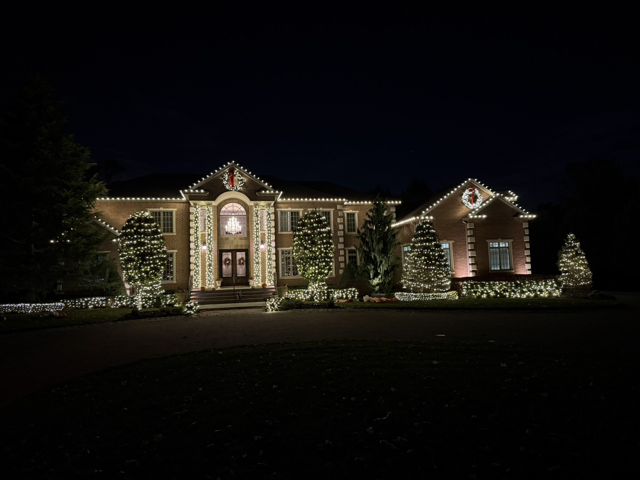 Wide view of a brick house with a warm white roofline and wrapped evergreens