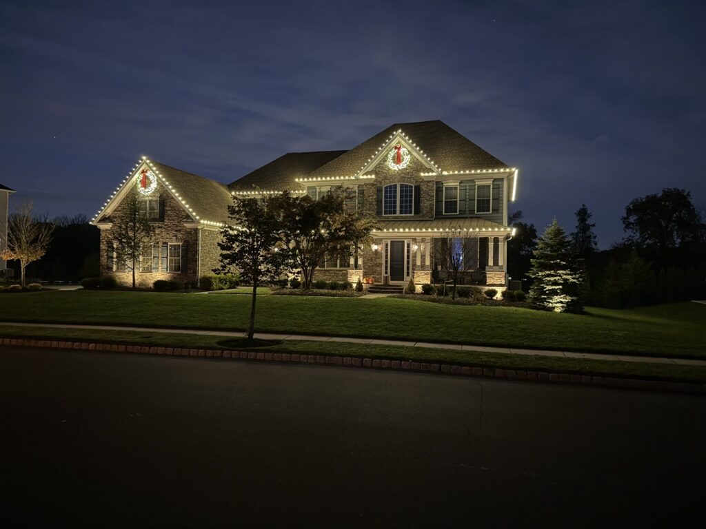 Colonial house with a warm white roofline and a lit wreath at blue hour