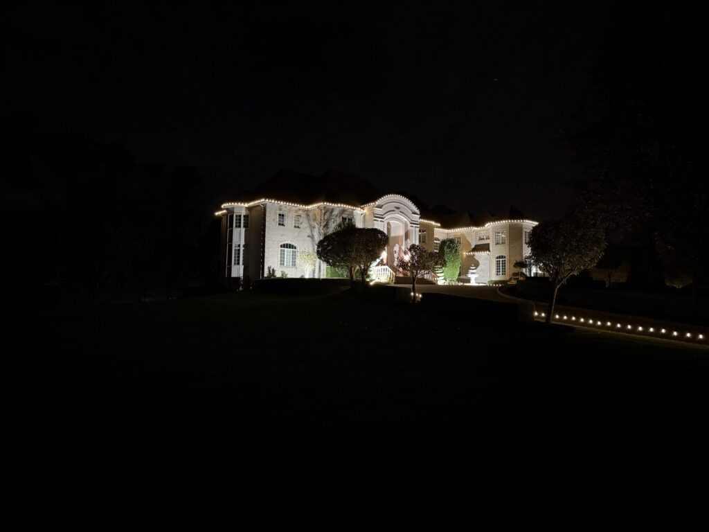 Large house with a warm white roofline and a lit driveway edge at night