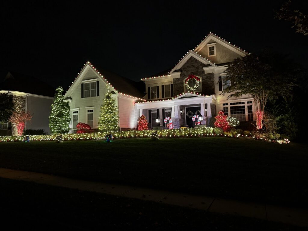 House with a warm white roofline, a lit wreath and red and green wrapped trees