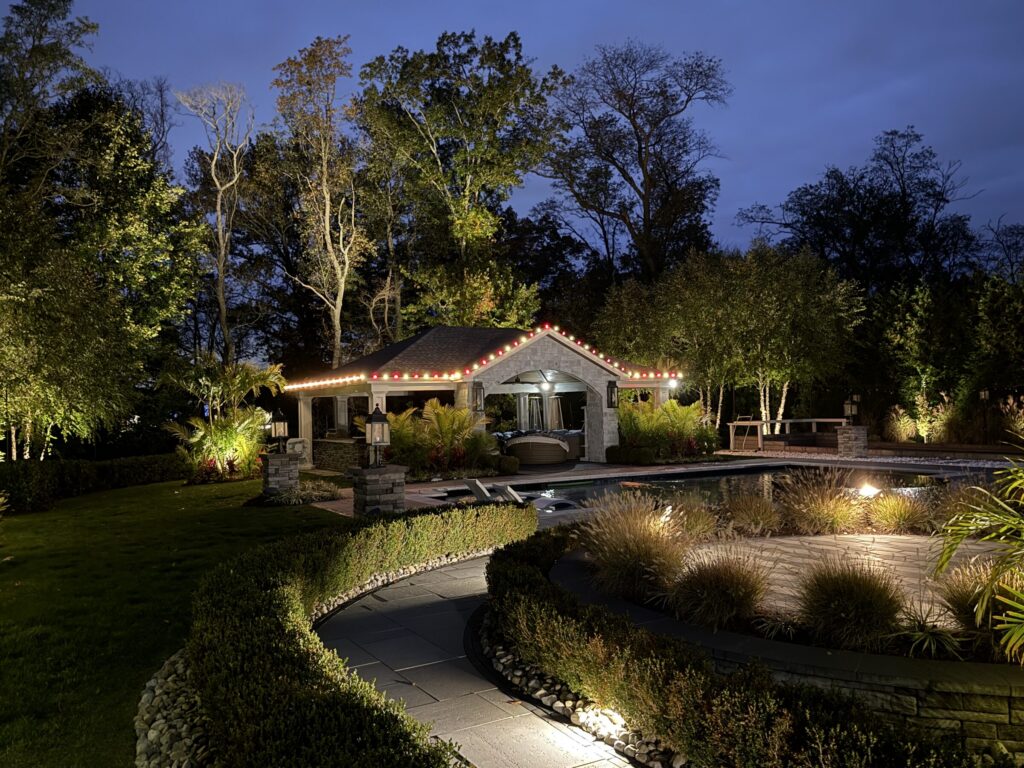 Pool house outlined in red and warm white lights beside lit landscaping at dusk