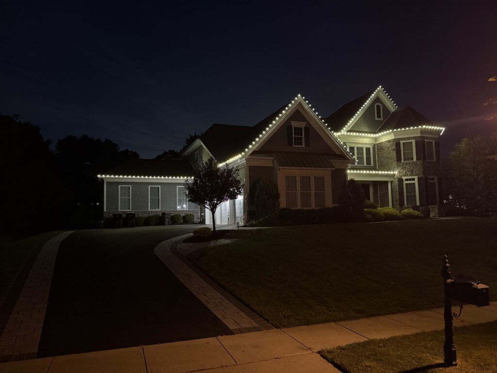 Shingle colonial with a warm white roofline at night