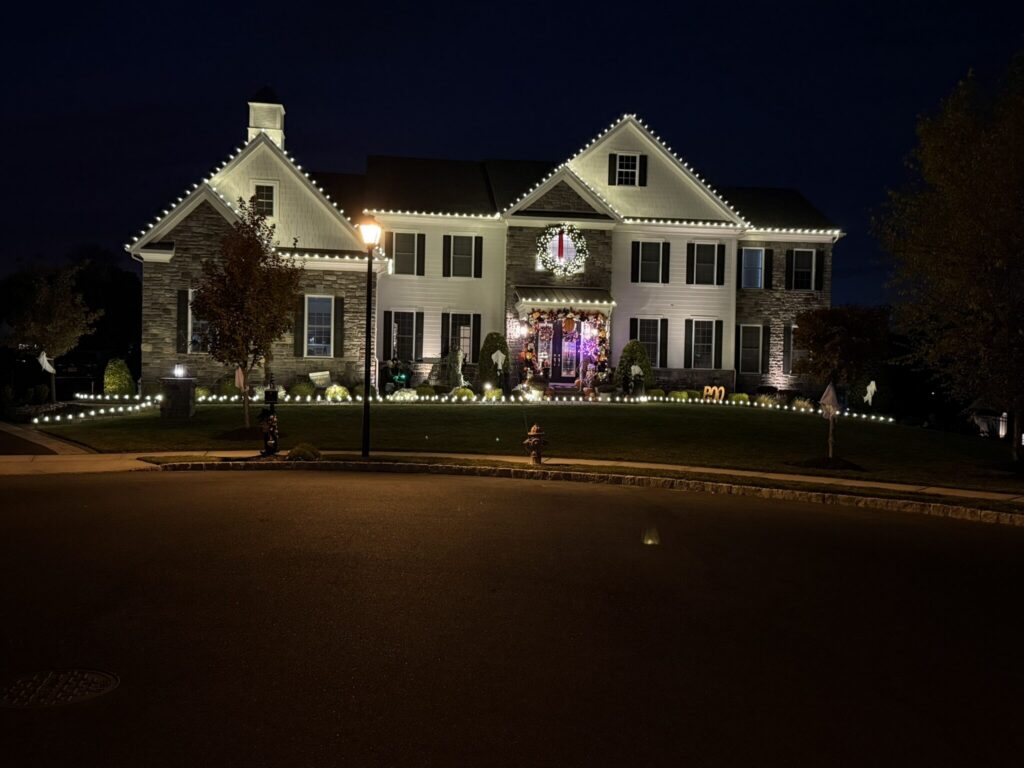 Stone and siding colonial with a warm white roofline and landscape lights at night