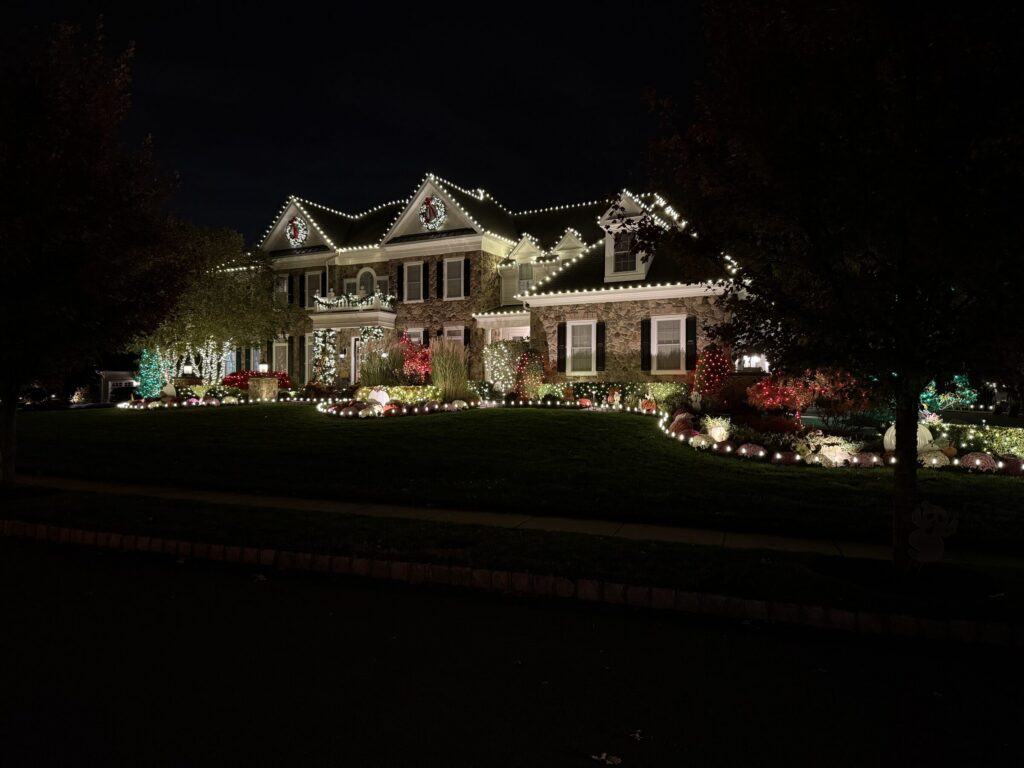 Stone colonial with a warm white roofline, wreaths and colored accent lights at night