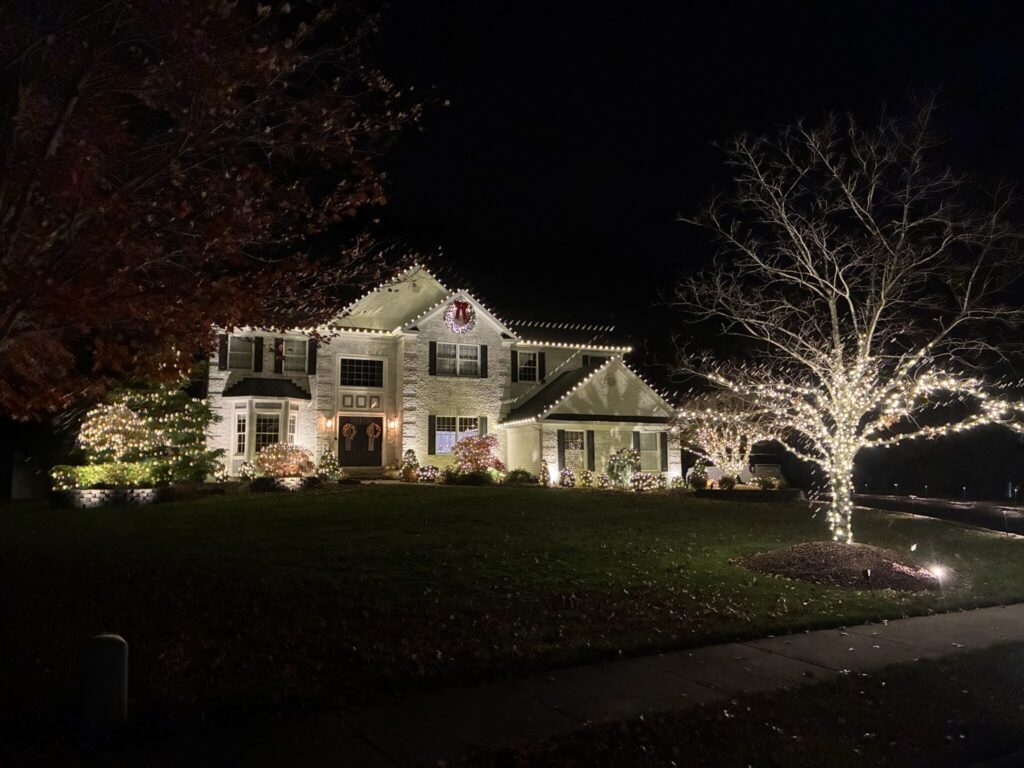 House with a warm white roofline and a tree wrapped in warm white lights