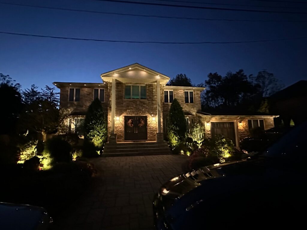 Stone house with a warm white permanent roofline and landscape lighting